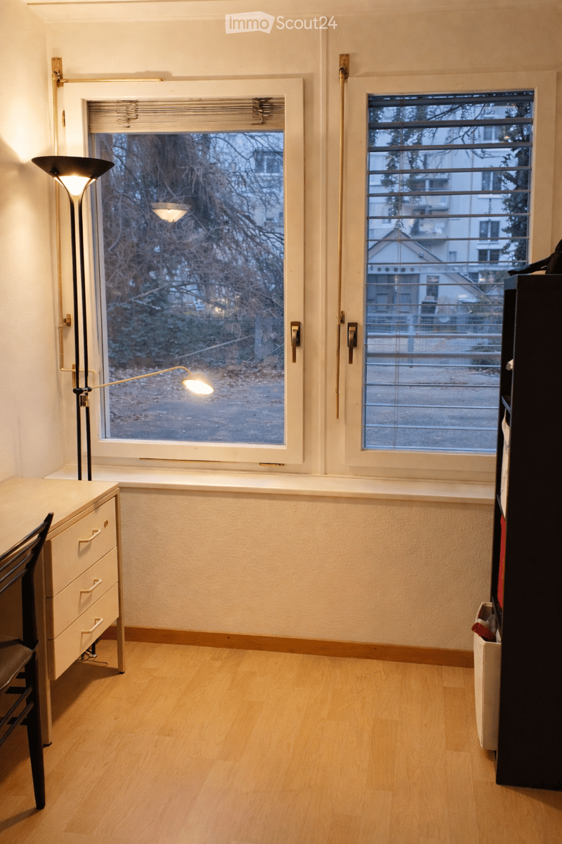 window with large window sill, floor lamp, desk with drawers, and two trash bins
