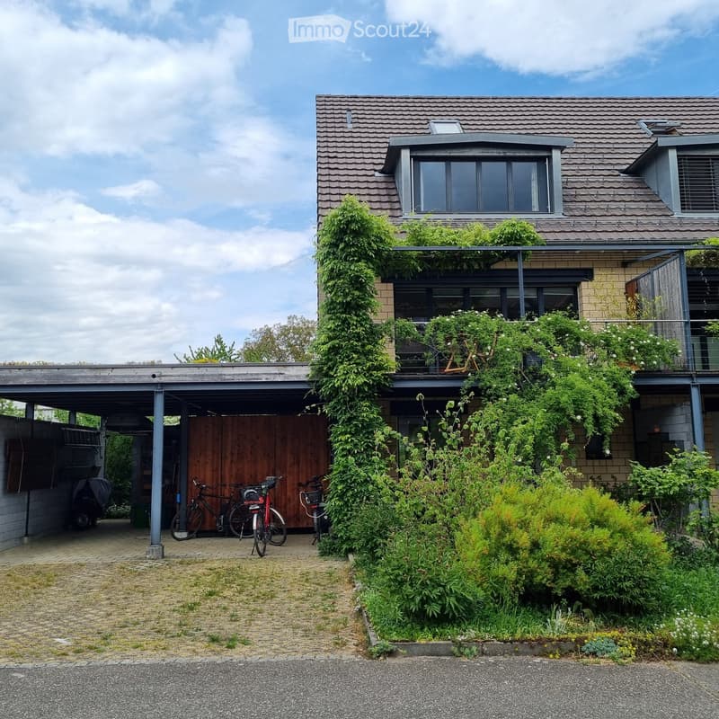 Two-story house with a tiled roof, covered garage, and balcony with greenery. Bicycles are parked under the garage.