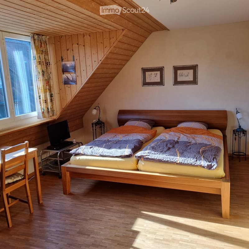 Bedroom with two beds, wooden headboards, wooden floor, wooden desk, wooden chair, lamp, TV, picture frames, curtains, window