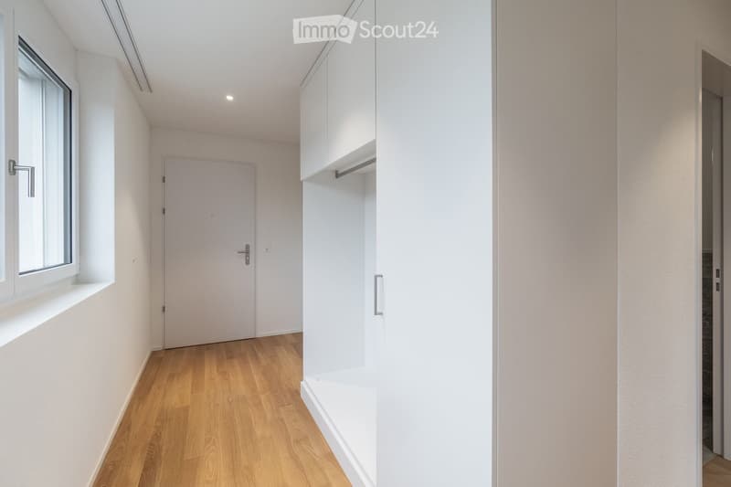 Empty hallway with wooden floor, white walls, white cabinets, and a window.