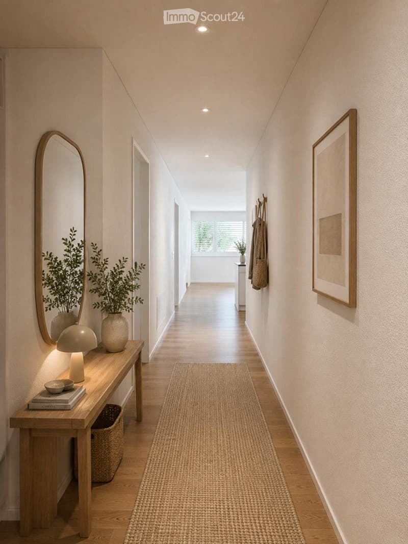 A modern hallway with light wooden flooring, white walls, recessed lighting, and a small console table with a mirror, plants, and decorative items. A woven runner rug is placed on the floor.