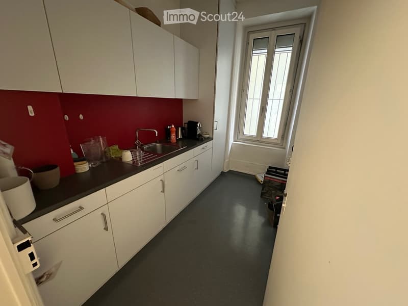 Modern kitchen with white cabinets, dark countertops, and a red backsplash. Includes a sink, faucet, coffee maker, and various small items on the counter.