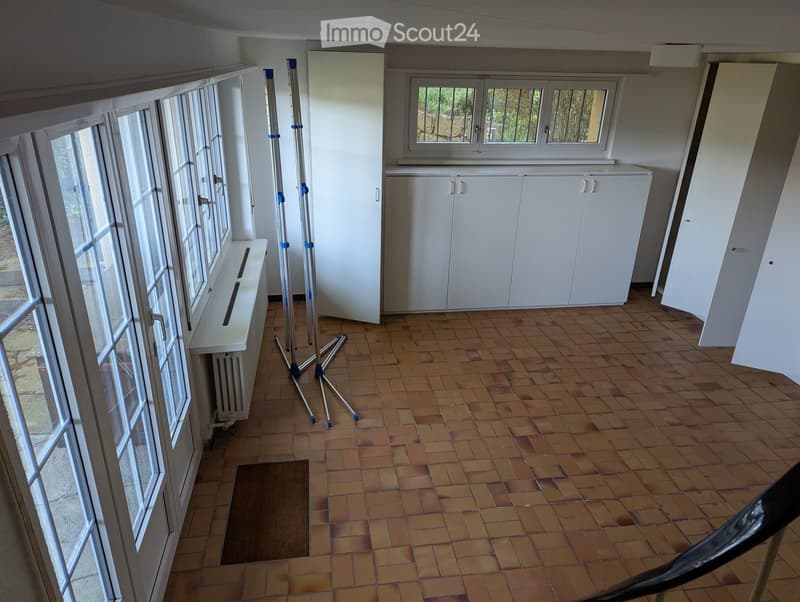 Empty room with tiled floor, white cabinets, large windows, radiator, and a tripod stand.
