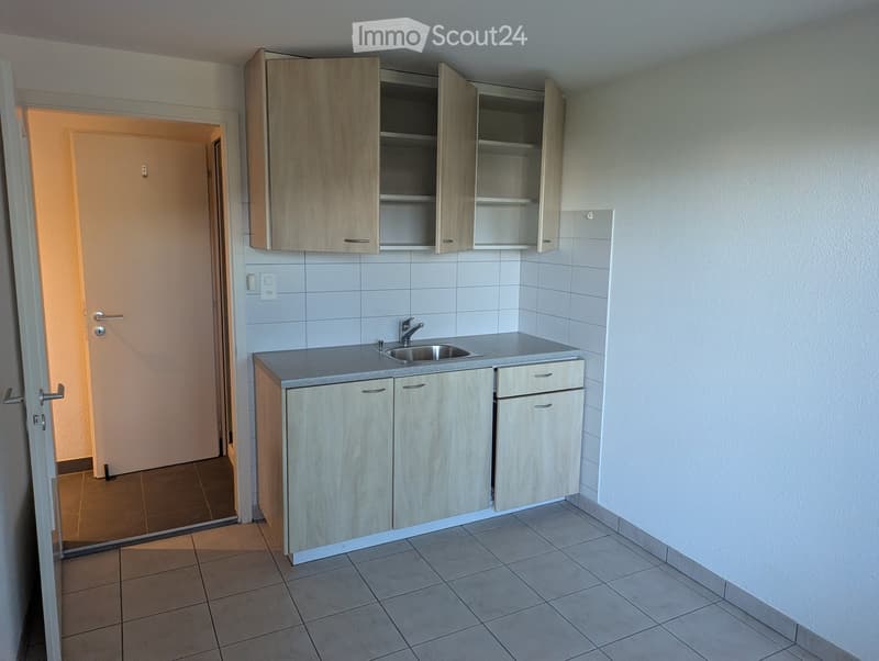 Empty kitchen with light wood cabinets, a sink, and tiled floors.