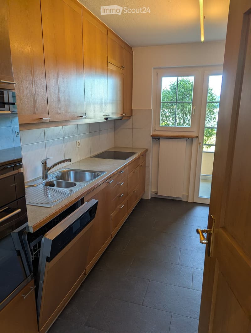 Modern kitchen with wooden cabinets, stainless steel sink, oven, and dishwasher. Light-colored countertops and tiled backsplash.