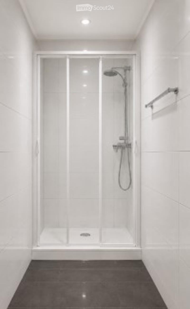 Modern bathroom with a large, enclosed shower stall featuring a sleek, contemporary design. The shower stall has a glass enclosure and a modern showerhead. The bathroom features white tiles and a dark, polished floor.