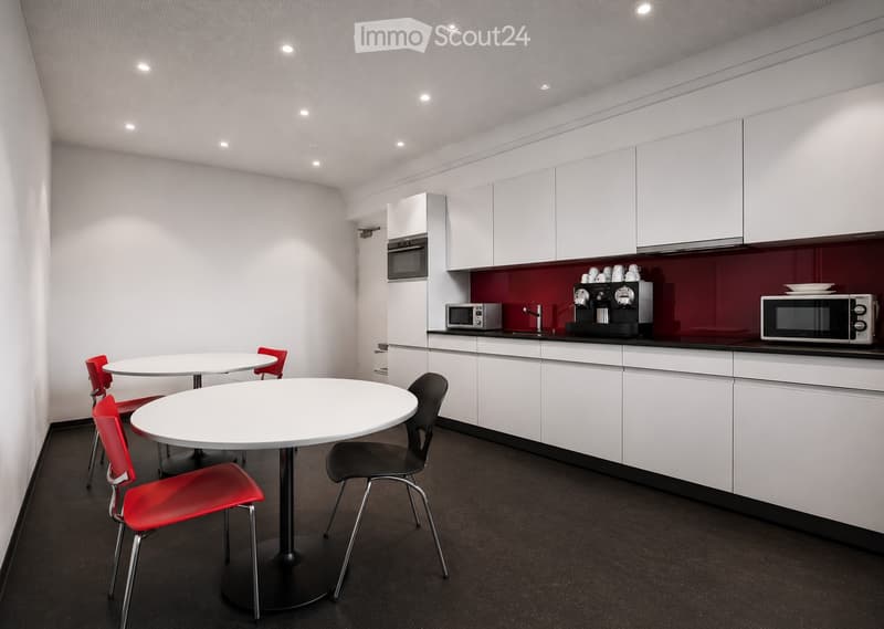 Modern kitchen with white cabinets, red accent wall, two round tables with chairs, microwave, oven, coffee machine, and faucet.