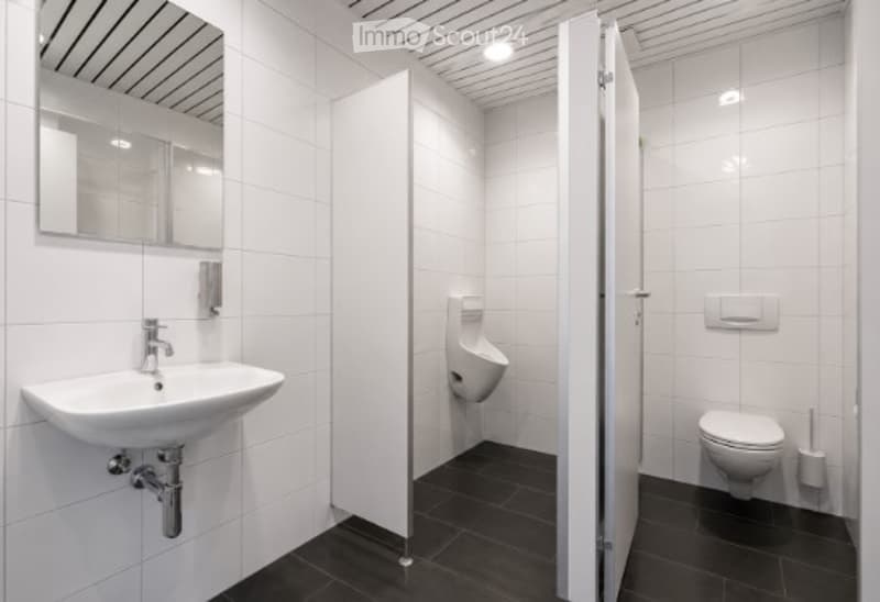 Modern bathroom with white tiles, black floor, sink, mirror, urinal, toilet, and toilet brush.
