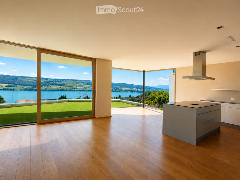 Modern kitchen with wooden flooring, large windows offering scenic views, kitchen island, and range hood.
