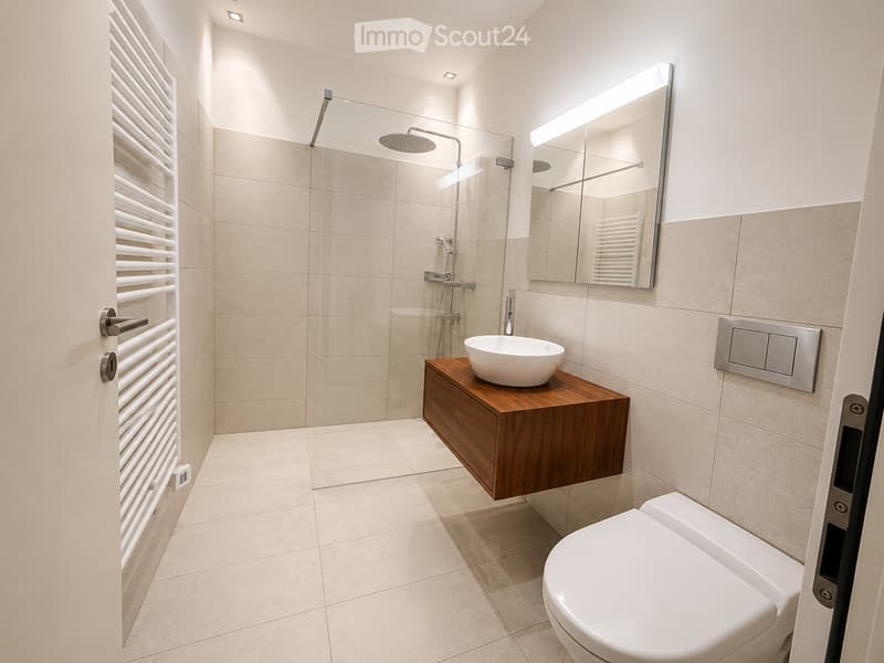 Modern bathroom with beige tiles, a white toilet, a wooden sink cabinet with a round sink, a large mirror with built-in lighting, and a glass-enclosed shower area with a rainfall showerhead.