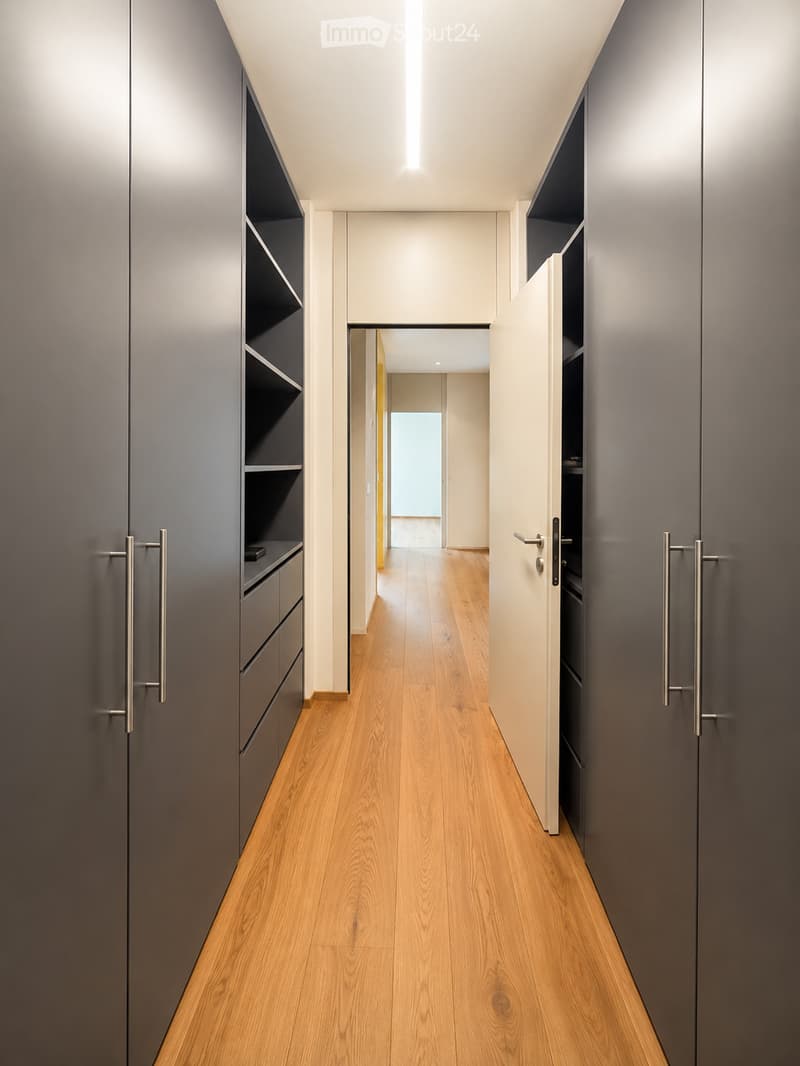 Modern hallway with light wooden flooring, grey built-in storage units with metallic handles, and recessed lighting.