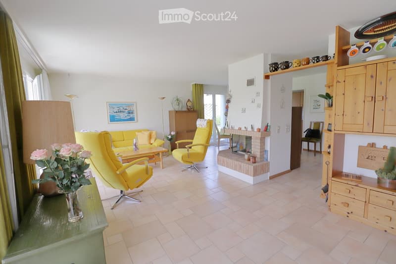 Bright living room with tiled flooring, yellow sofa, armchairs, coffee table, fireplace, and wooden cabinetry.