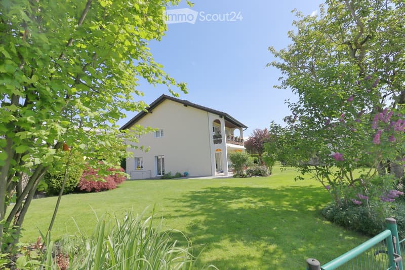 Two-story house with a balcony, surrounded by a well-maintained lawn and trees.