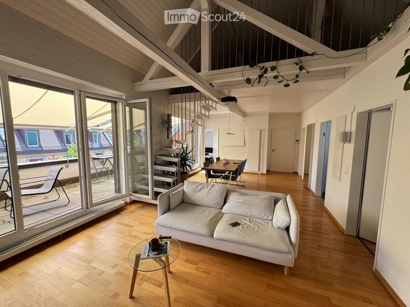 Bright living room with wooden flooring, white sofa, glass coffee table, dining area with table and chairs, and large sliding glass doors leading to a balcony.