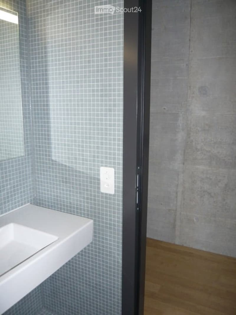 Empty bathroom with tiled walls, a white sink, and a wooden floor. No furniture or fixtures are present.
