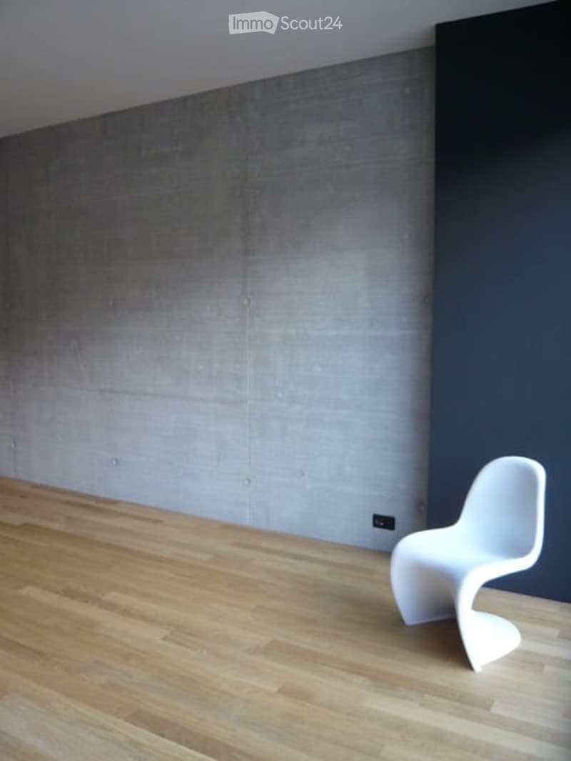 Minimalist room with light wooden flooring, grey textured wall, and a single white modern chair.