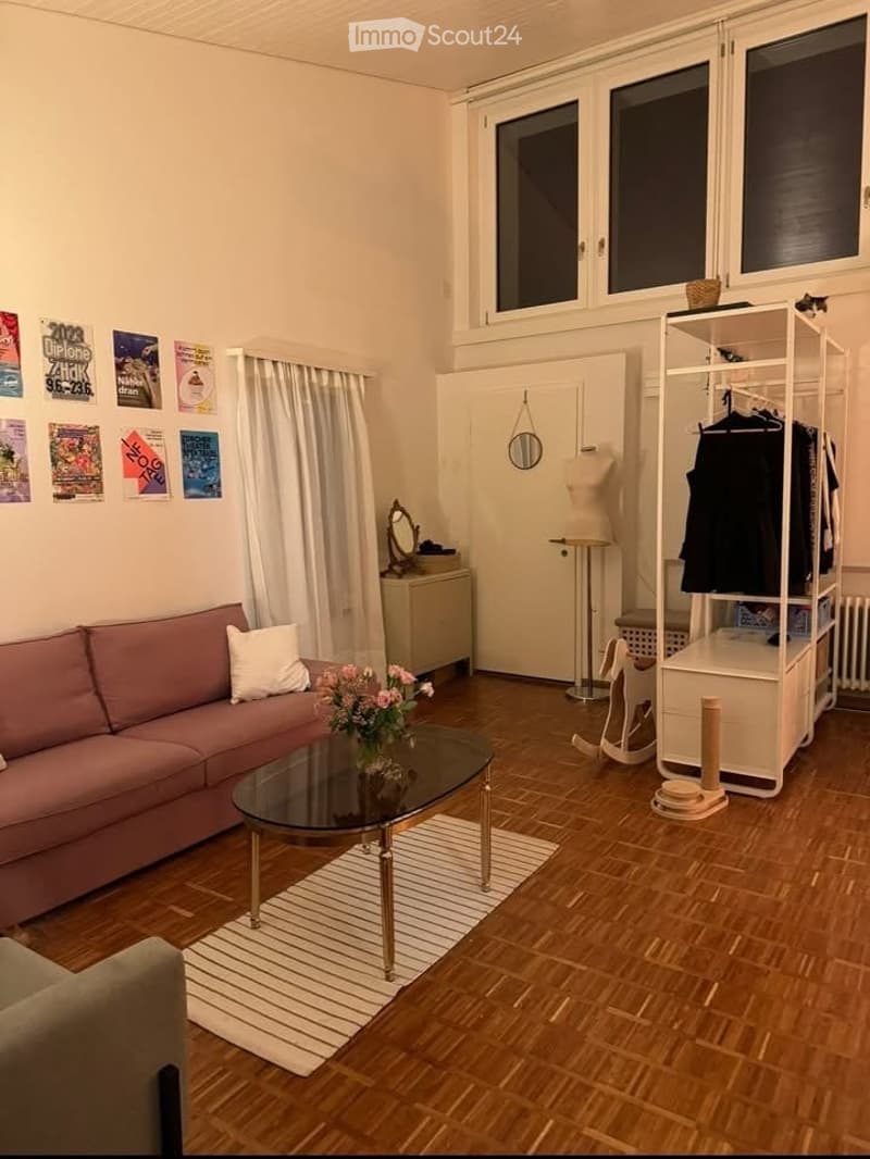 A cozy living room with a pink sofa, glass coffee table, flower vase, mirror, wardrobe, shelf, rocking horse, and cat tree. The room features wooden flooring and large windows with curtains.