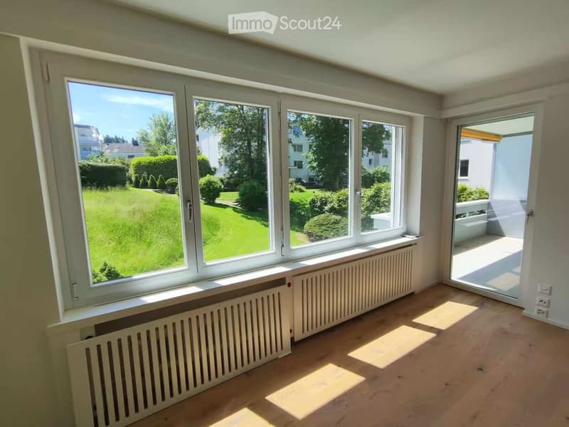 Empty room with wooden flooring, large windows, radiators, and a sliding glass door leading to a balcony or terrace.