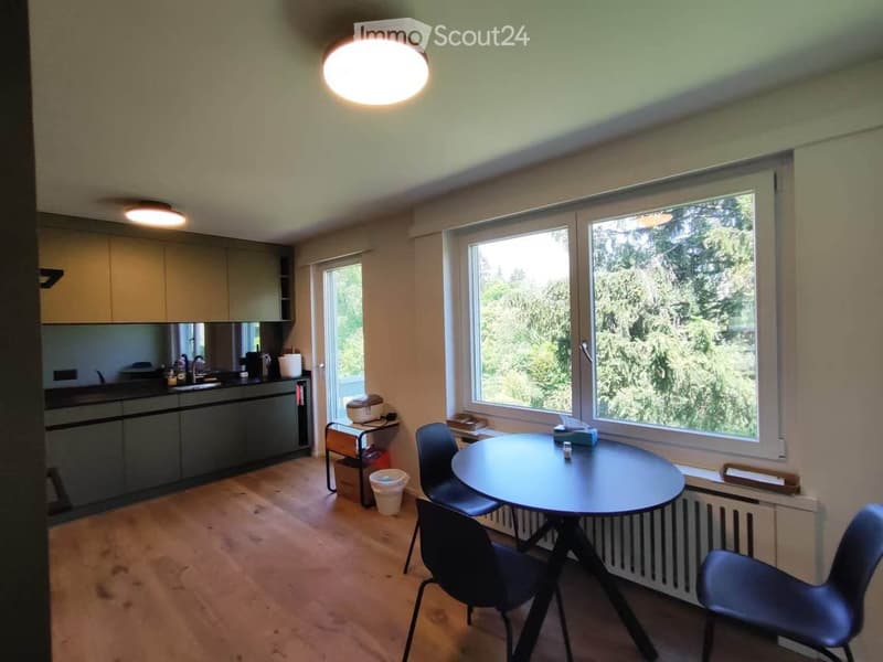 Bright, modern kitchen and dining area with wooden flooring, large windows, and contemporary furniture including a round dining table and chairs.