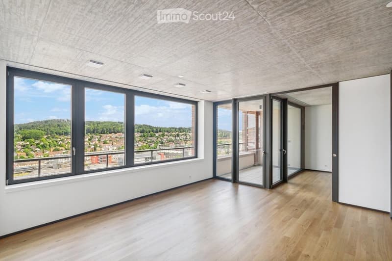 Empty room with wooden flooring, large windows, and sliding glass doors leading to a balcony.