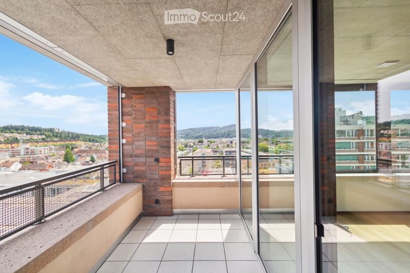 Modern balcony with large glass doors, tiled floor, metal railing, and scenic city view.
