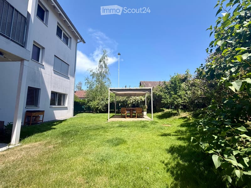 Well-maintained garden with a wooden pergola, outdoor dining set, and lush greenery surrounding the area.