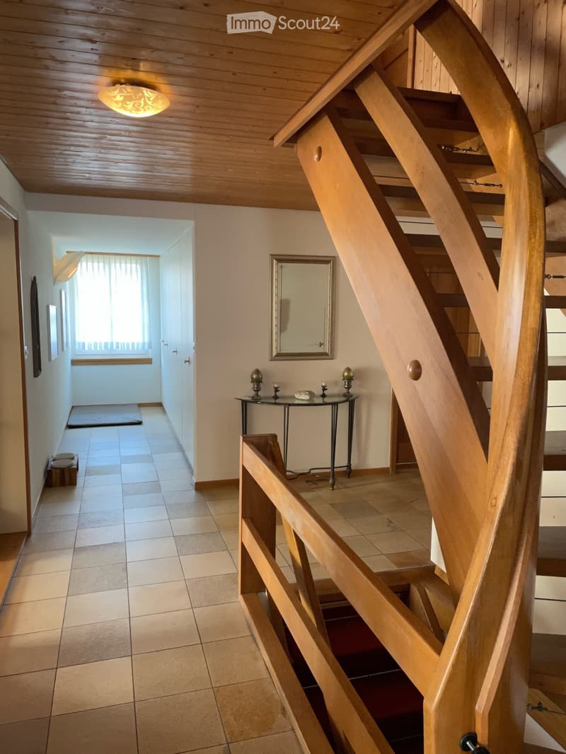 Spacious hallway with wooden staircase, tiled floor, and a small glass table with decorative items near the stairs.