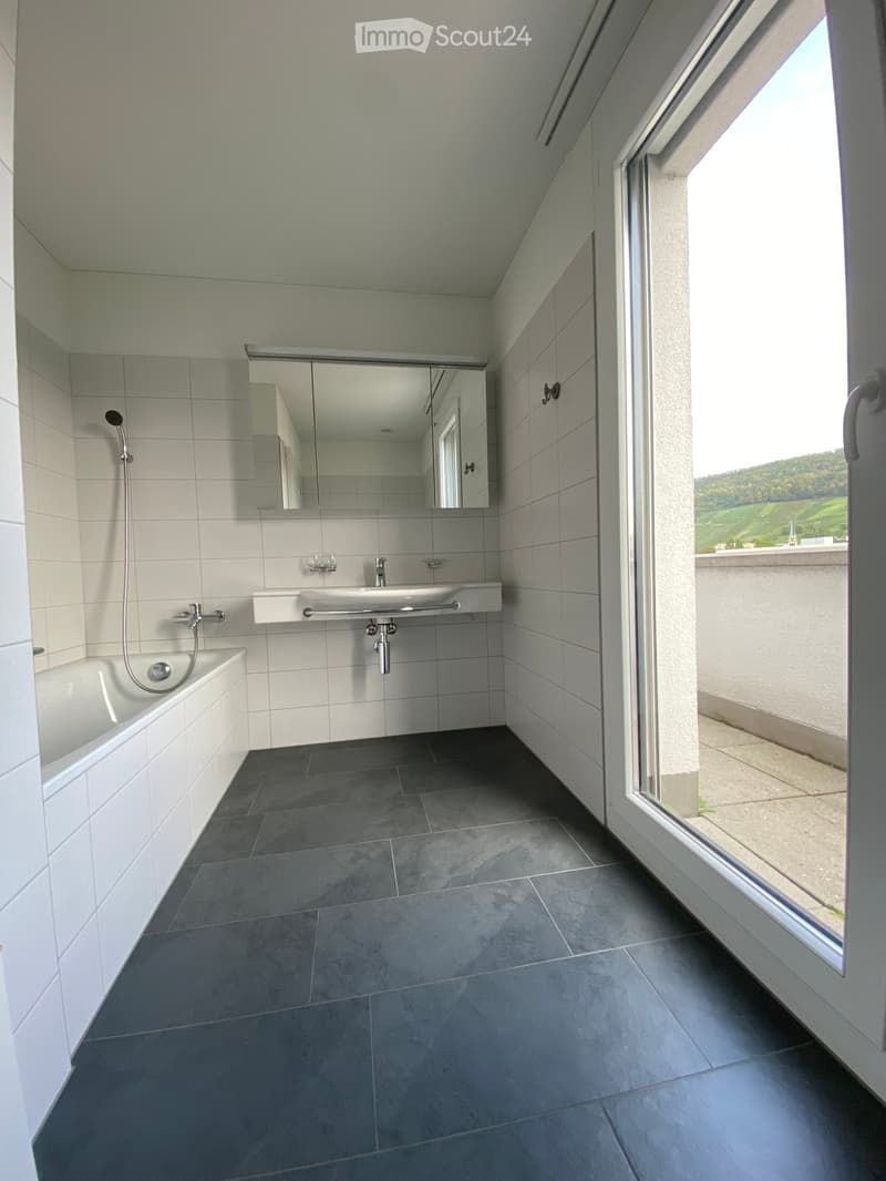 Modern bathroom with a bathtub, sink, mirror, and large window offering a scenic view.