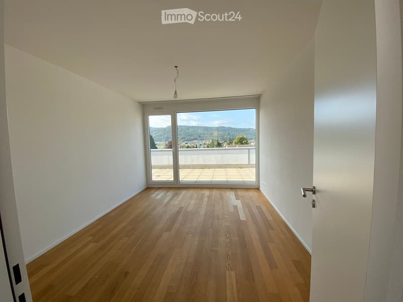 Empty room with wooden flooring, white walls, and large windows offering a scenic view of a landscape.
