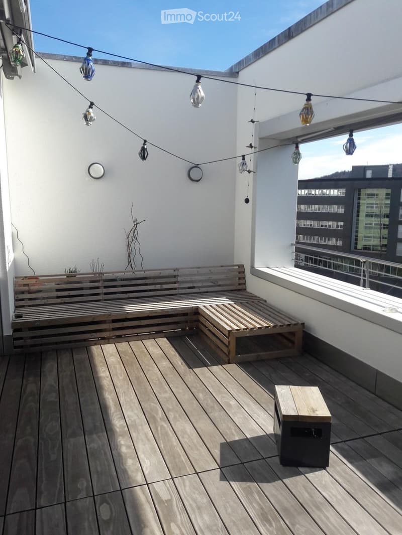 Wooden deck with a bench, stool, string lights, and a small plant in the corner.