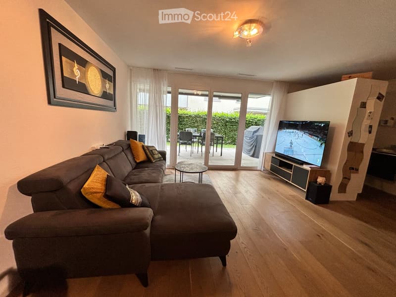 Modern living room with a sectional sofa, coffee table, TV, and large windows leading to a patio.