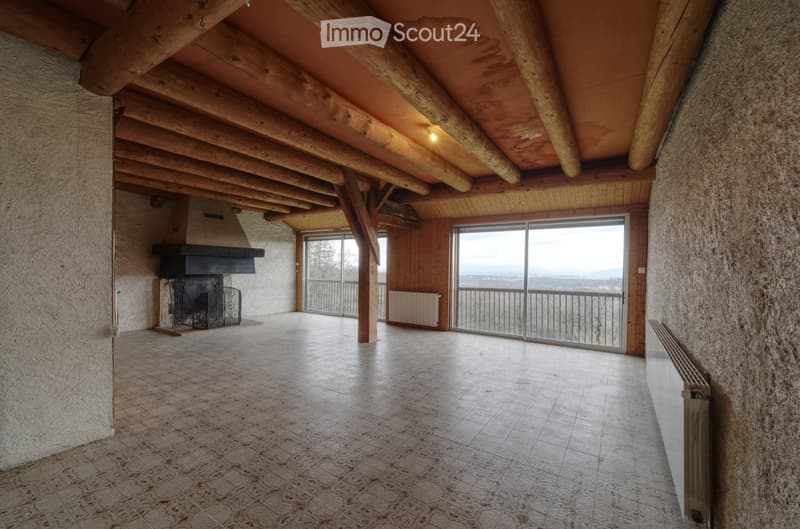 An unfurnished room with exposed wooden beams, a fireplace, large windows, and a balcony view.