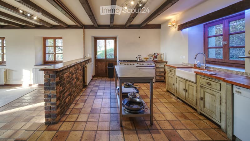 Spacious kitchen with exposed wooden beams, brick counter, wooden island, stainless steel sink, stove, and various kitchen utensils.