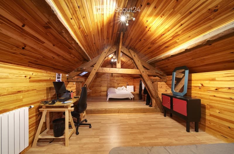 Cozy attic bedroom with wooden walls and ceiling, featuring a bed, desk with computer, chair, mirror, dresser, and nightstand.