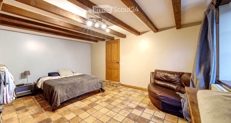 Cozy attic bedroom with wooden beams, tiled floor, bed, sofa, nightstand, and lamp.