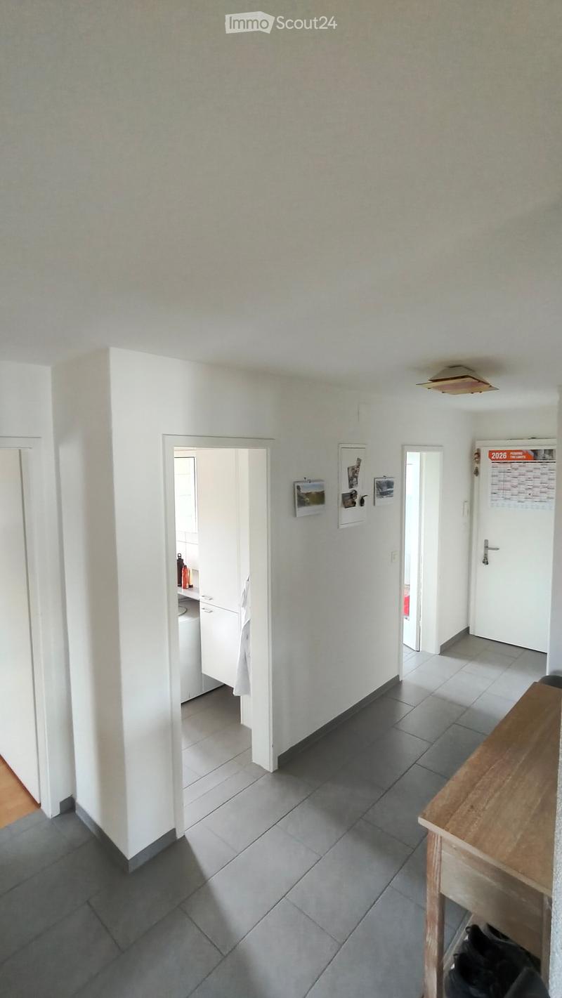 Empty hallway with grey tiled floor, white walls, and several doors leading to other rooms. A small wooden table is visible on the right side.