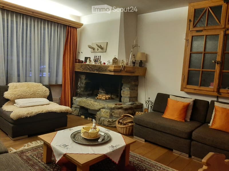 Cozy living room with a stone fireplace, two sofas, a coffee table with a decorative runner, and a basket of firewood.