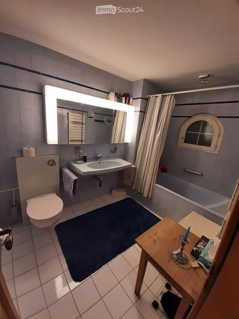 Bathroom with a toilet, sink, mirror, bathtub, and a small wooden table with a candle and other items.