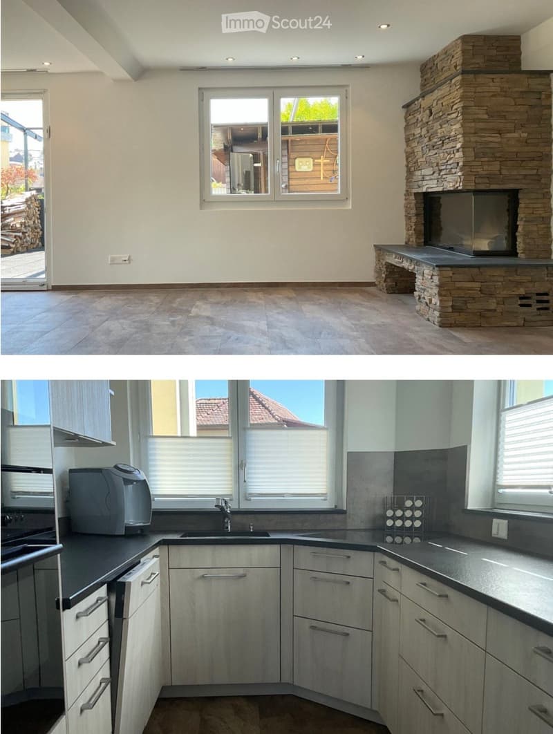 Modern kitchen with light grey cabinets, black countertops, a sink, a coffee maker, and a wine rack. The room features large windows and a stone fireplace in the adjacent living area.