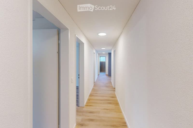 Empty hallway with white walls, wooden floor, and ceiling lights