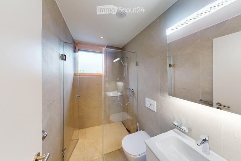 Modern bathroom with glass shower, white sink, white toilet, beige tiles, mirror, and a window