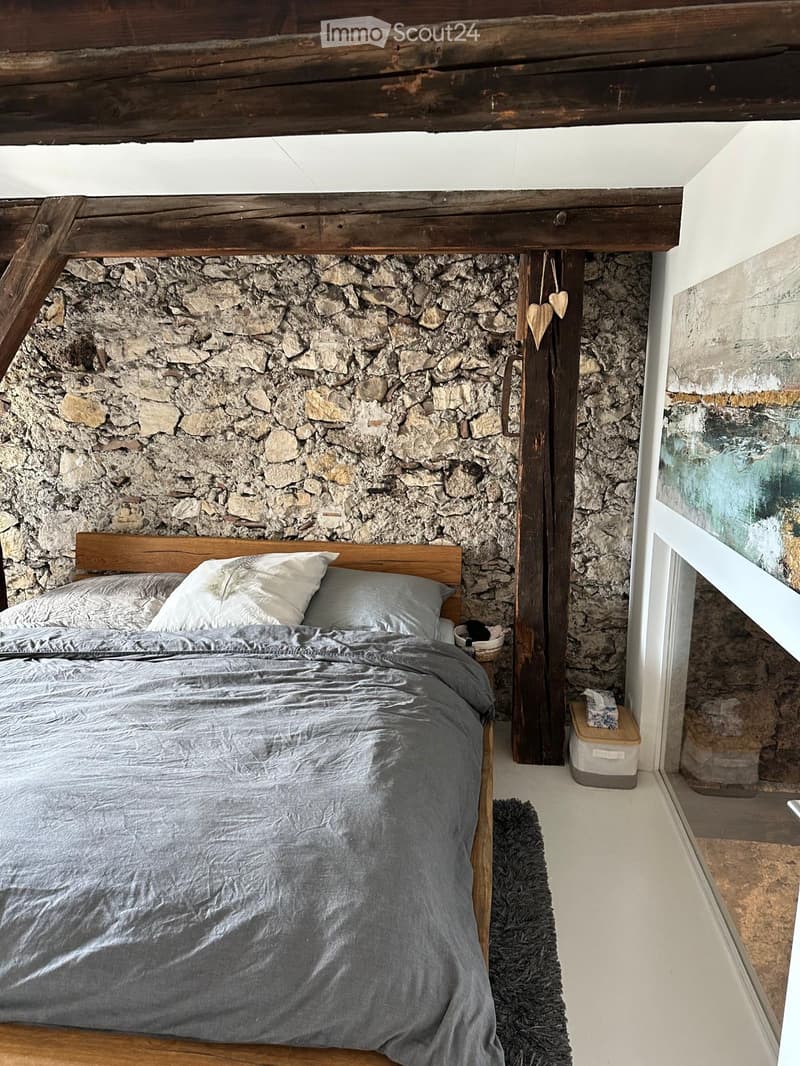 Cozy bedroom with a wooden bed, stone accent wall, and a small nightstand with a basket on top.