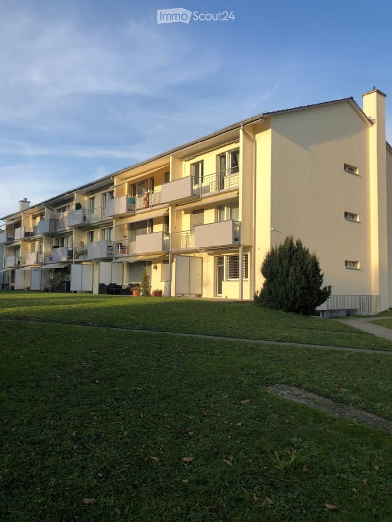 Multi-story residential building with multiple balconies and a well-maintained lawn in front.