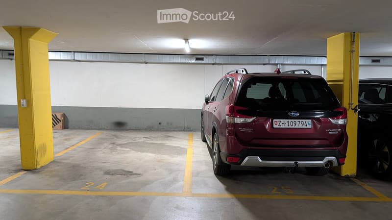 Underground parking area with marked parking spaces, featuring a red Subaru Forester and a black car, with yellow pillars and concrete floors.