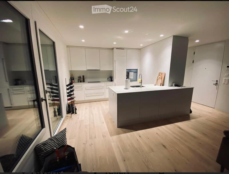 Modern kitchen with white cabinets, a central island, and wooden flooring. Features include a sink, faucet, wine rack, and various appliances.