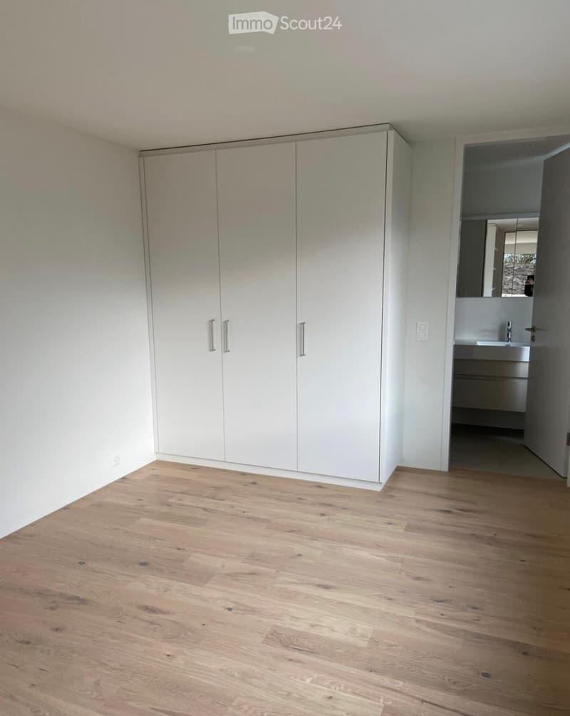 Empty room with light wooden flooring, white built-in wardrobes, and an open doorway leading to a bathroom.