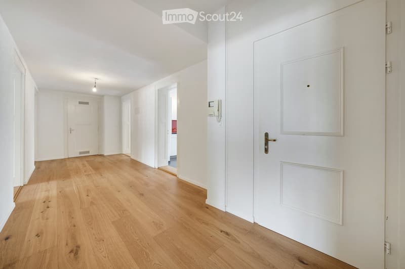 Empty hallway with light wooden flooring, white walls, and several white doors.