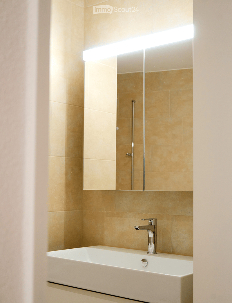 Modern bathroom with a white sink, chrome faucet, and large mirror with built-in lighting.