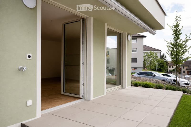 Balcony with large sliding glass doors, tiled floor, and a view of a residential area with parked cars and greenery.