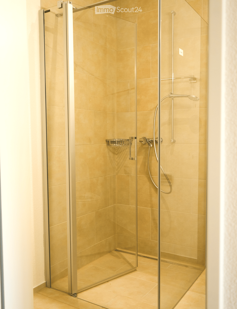 Modern bathroom with a glass-enclosed shower stall, beige tiles, and a sleek shower handle.